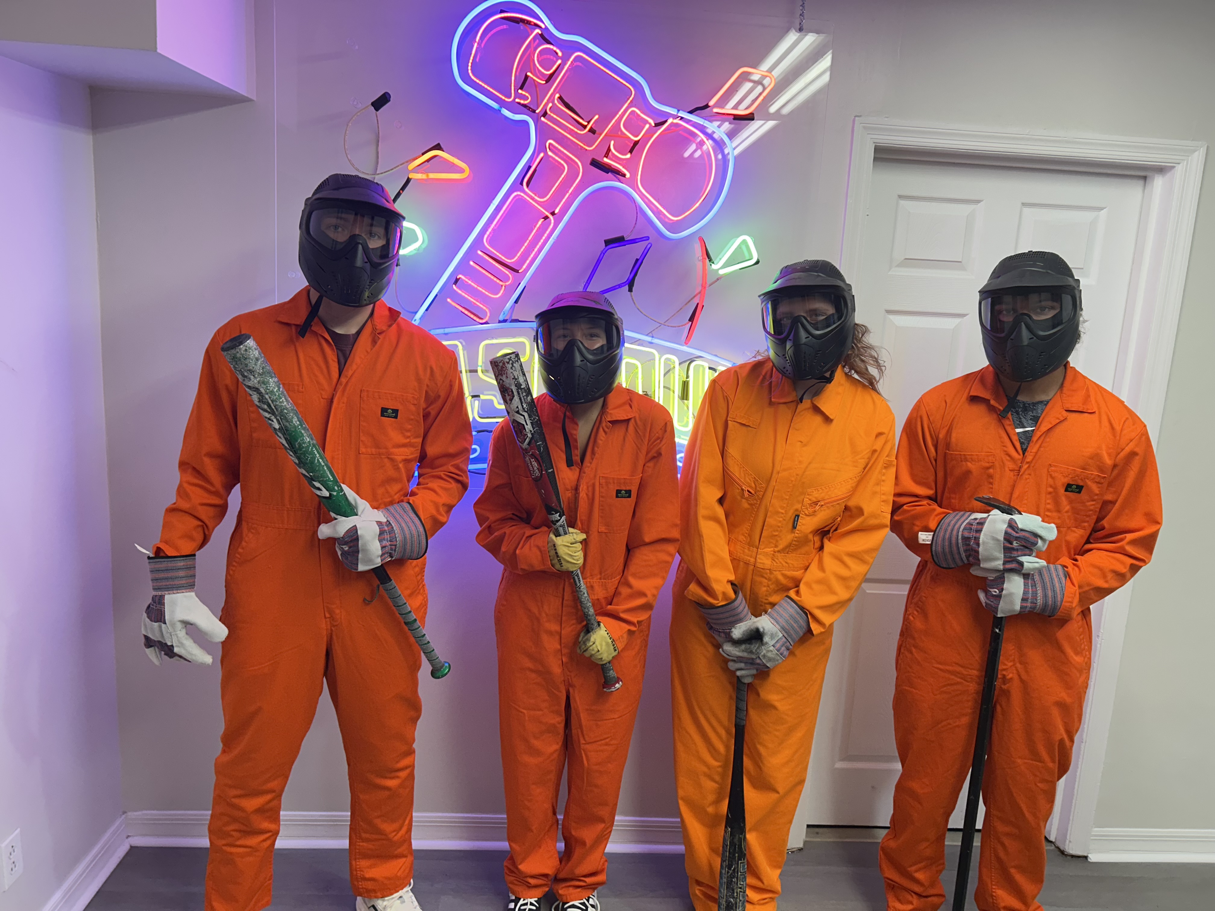 Crash Out customers in orange jumpsuits selecting bats from barrel of smash tools