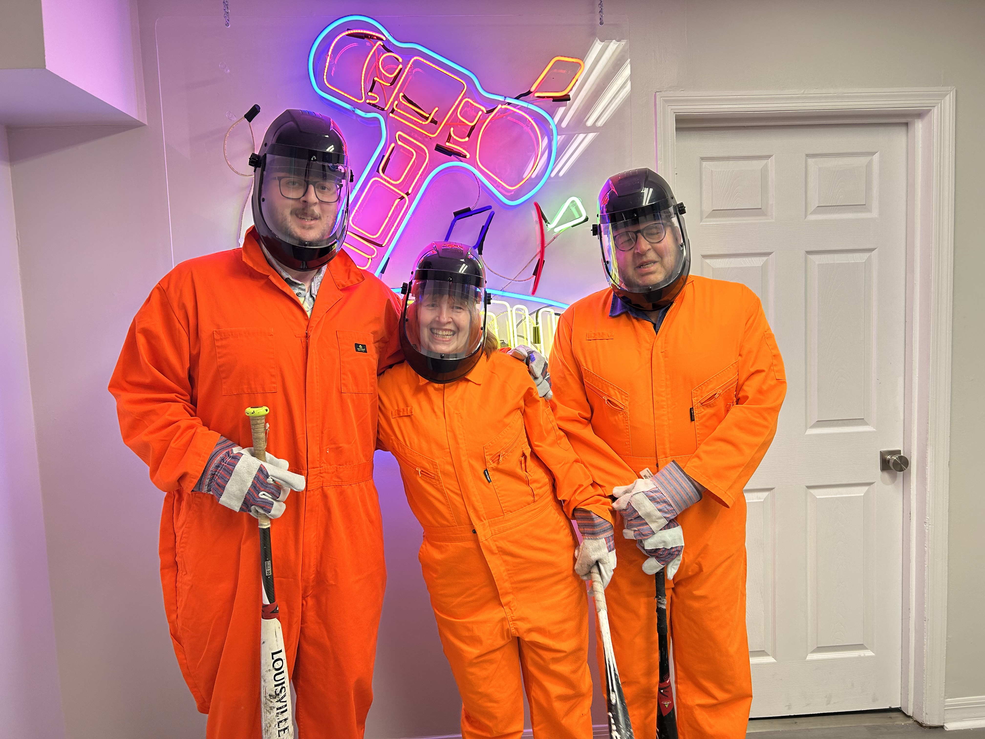 Three Crash Out guests in orange jumpsuits smiling and ready to enter the smash room