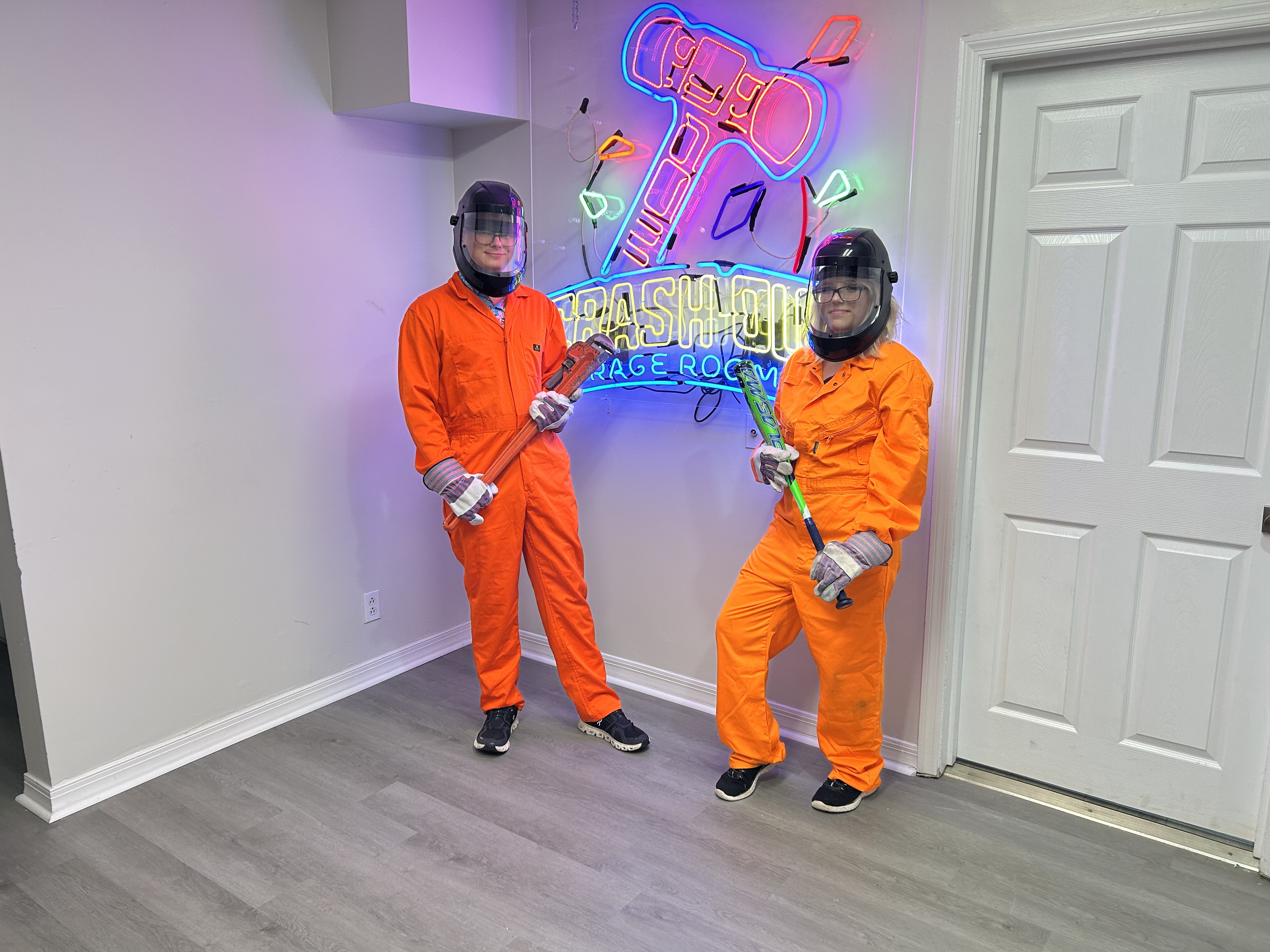 Large group of Crash Out customers in orange jumpsuits and protective gear with bats in front of branded neon sign