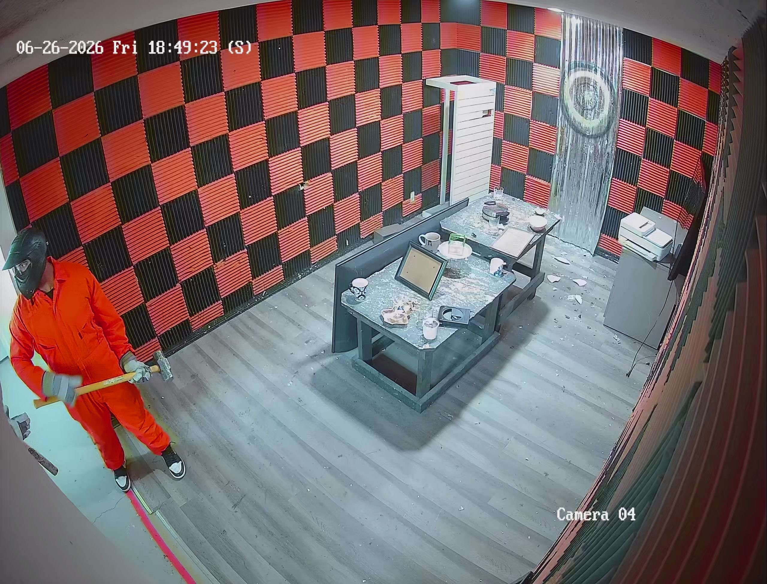Security camera footage of Crash Out Rage Rooms guest in orange jumpsuit mid-smash inside red and black checkered rage room