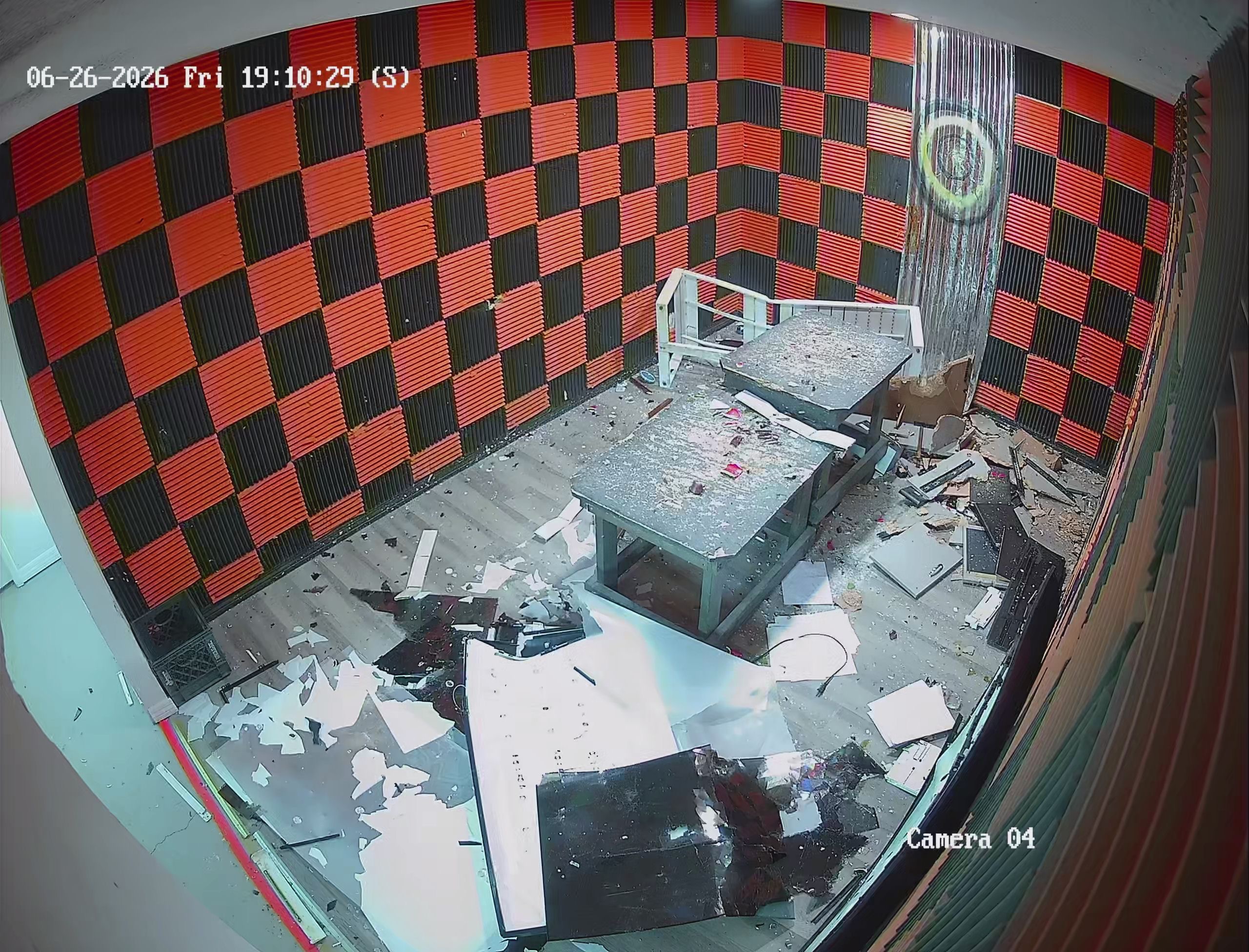 Security camera view of Crash Out rage room aftermath — floor covered in shattered glass, electronics, and debris